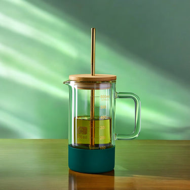 Elegant 600mL glass beaker tumbler with a bamboo lid, gold metal straw, and a dark green silicone base, combining scientific charm with modern drinkware functionality.