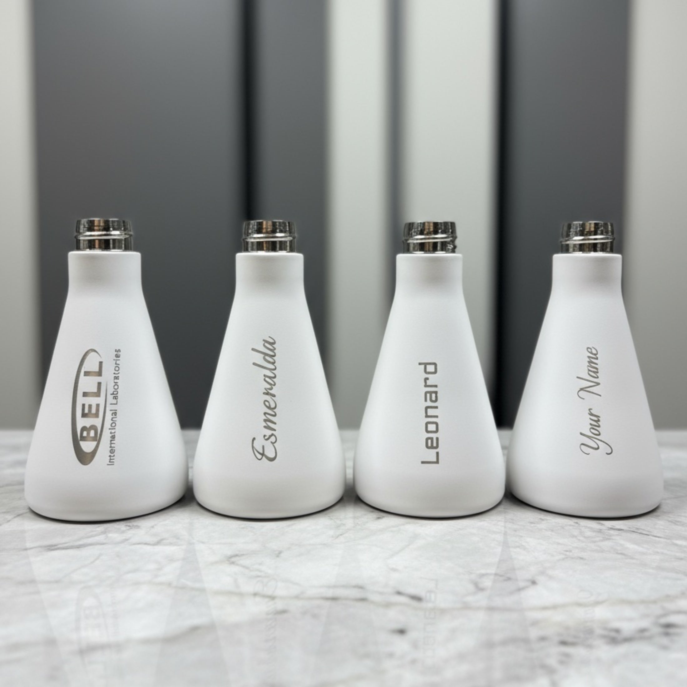 Four white bottles with engraved names on a marble surface